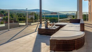 A covered outdoor seating area with wicker furniture and a glass balustrade overlooking a scenic landscape. - Luxurious home in Dubrava kod Sibenika (Dubrava kod Sibenika)