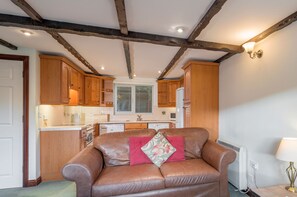 A cozy living room with a leather sofa, wooden cabinets, and a kitchen in the background.