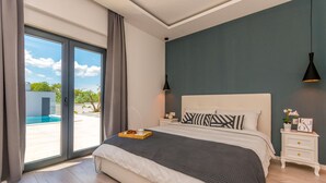 Een slaapkamer met een groot bed, een nachtkastje, een raam met gordijnen en uitzicht op een buitenzwembad.