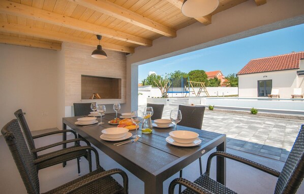 A dining area with a table set for four, outdoor seating, a brick fireplace, and a view of the street and buildings. - Beautiful home in Skabrnja (Skabrnja)