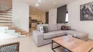 Een moderne woonkamer met een grijze modulaire bank, een houten salontafel en een trap naar een verdieping erboven.