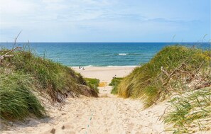 Un sentier de sable qui longe la plage et mène à l’océan, avec des dunes herbeuses de chaque côté.