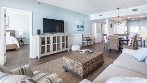 A spacious living room with a large flat-screen TV, wicker furniture, and a dining area with wicker chairs.