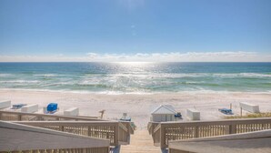 A beach view with a wooden deck leading to the ocean, featuring beach chairs and umbrellas.