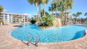A swimming pool with a 3 ft depth marker, surrounded by palm trees and a hotel building with multiple balconies.