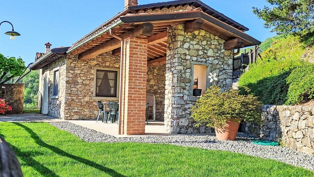 A stone house with a wooden porch, a chimney, and a small window. - Beautiful apartment in villa for 6 guests with pool, WIFI, TV and patio (Molazzana)
