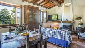 A rustic interior with a dining table set for two, a television mounted above a fireplace, and a cozy seating area with a checkered sofa. - Beautiful apartment in villa for 6 guests with pool, WIFI, TV and patio (Molazzana)