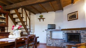 Un accogliente soggiorno con camino in pietra, arredi in legno, una scala e un televisore su una mensola.