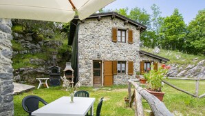 Un edificio in pietra con una porta in legno e finestre dotate di persiane, un tavolo con sedie e un recinto in legno.
