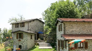Una casa in pietra con tetto in tegole, un piccolo portico con posti a sedere all'aperto e una scala che conduce all'ingresso.