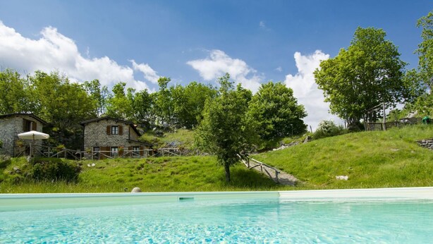 Una piscina con acqua cristallina, circondata da un edificio in pietra e vegetazione rigogliosa.