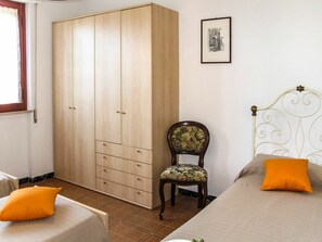 Ein Schlafzimmer mit großem Kleiderschrank, einem Sessel, zwei Betten mit orangefarbenen Kissen und einem gerahmten Bild an der Wand.