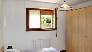 Une chambre à coucher avec un lit, une fenêtre donnant sur un beau paysage, une armoire et un radiateur.