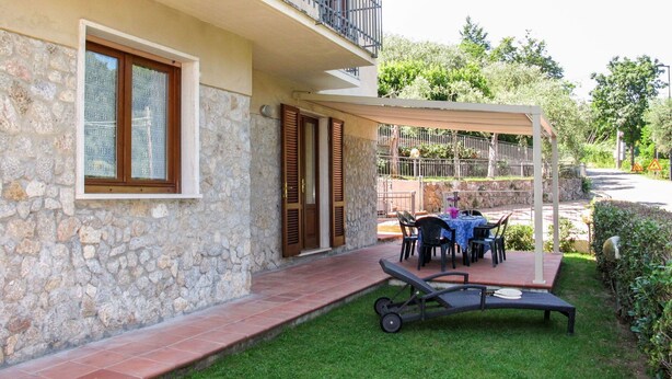 Un bâtiment à deux étages avec des murs en pierre, un balcon et un espace extérieur couvert aménagé avec une table et des chaises.