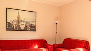 Une pièce avec un canapé rouge, un lampadaire et un tableau représentant un paysage urbain accroché au mur.