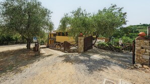 Una vila rústica amb una porta de pedra, envoltada d'oliveres i un camí de grava.