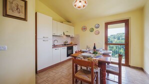 Zona de menjador amb una taula preparada per a quatre, cuina amb armaris blancs i vista a través d'una porta de vidre.