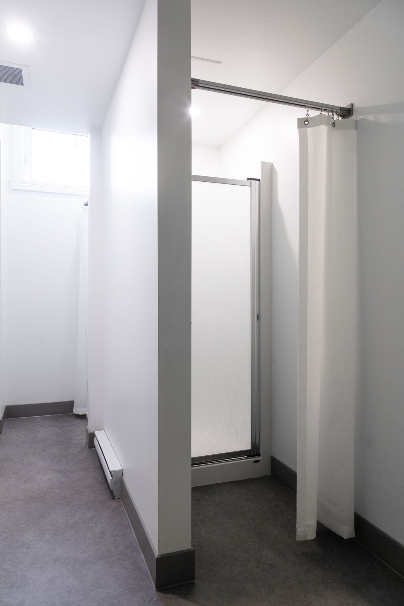 A narrow hallway with a shower stall, a radiator, and a door leading to another room.