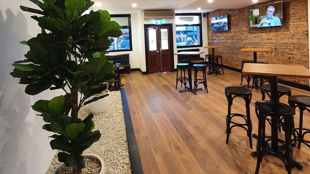 A modern indoor space with wooden flooring, a potted plant, and a television mounted on the wall. - Empire Hotel Goulburn (Goulburn)