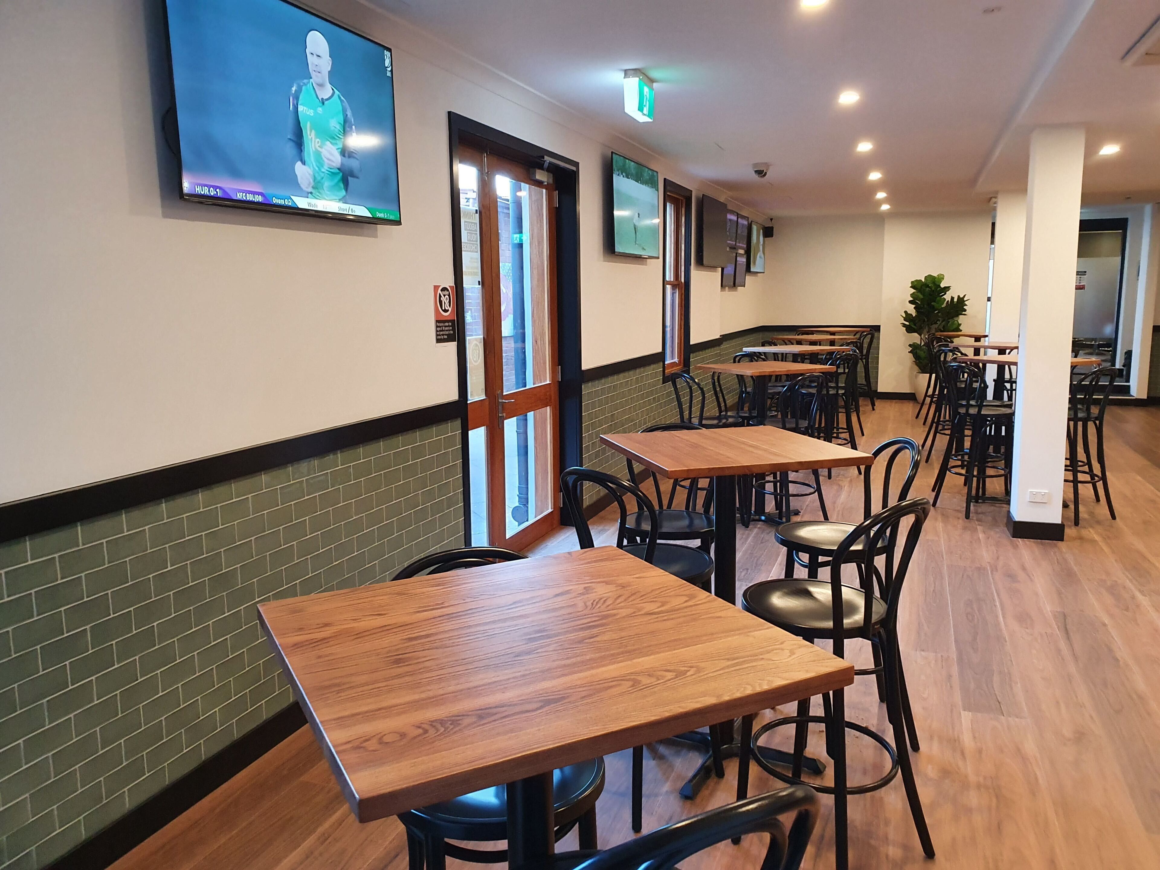 A restaurant with wooden tables and chairs, a TV mounted on the wall, and a brick wall.