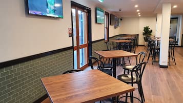 A restaurant with wooden tables and chairs, a TV mounted on the wall, and a brick wall.