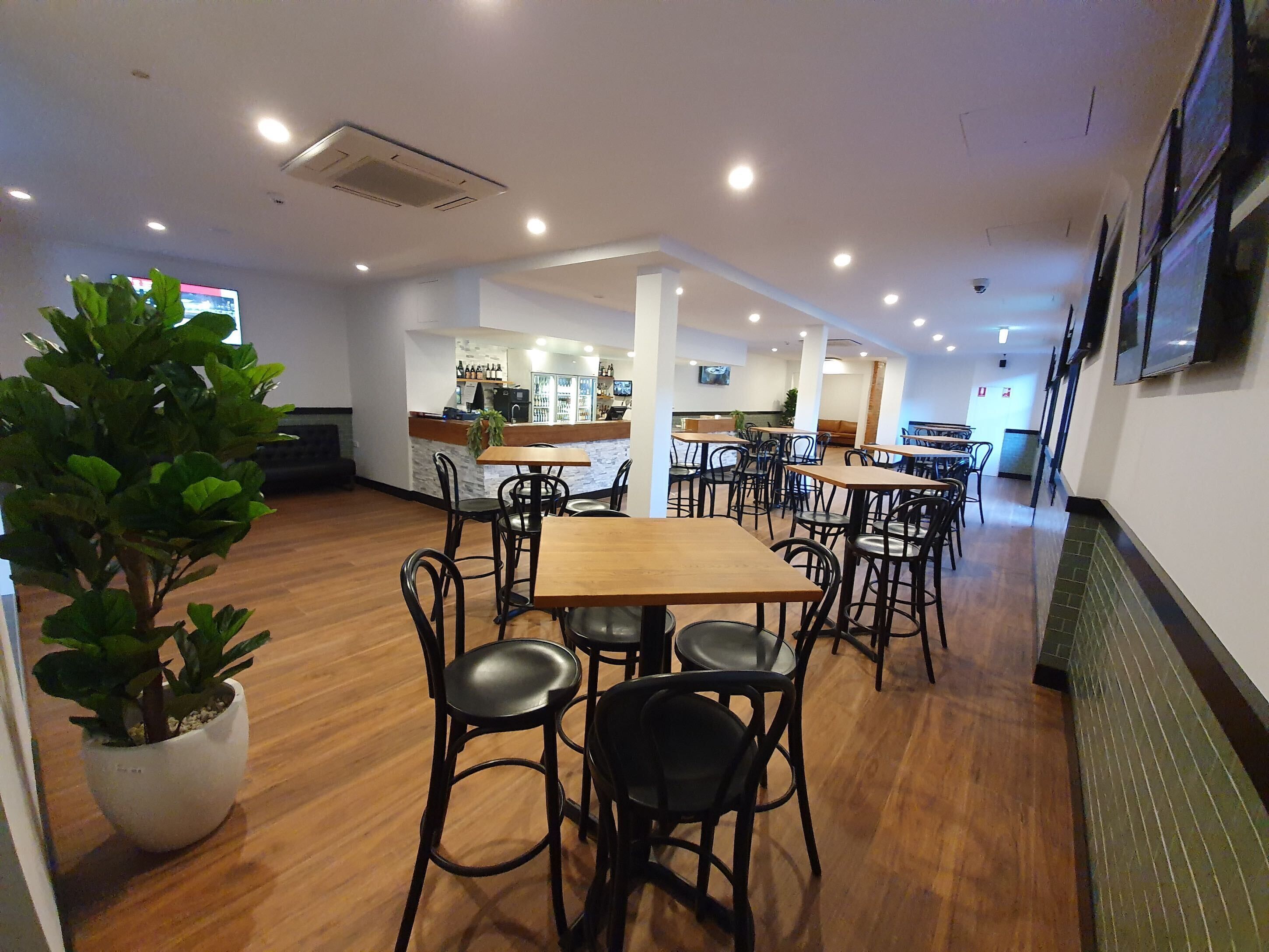 Un espacio interior amplio con suelo de madera, varias mesas y sillas, una zona de bar y una planta en maceta.