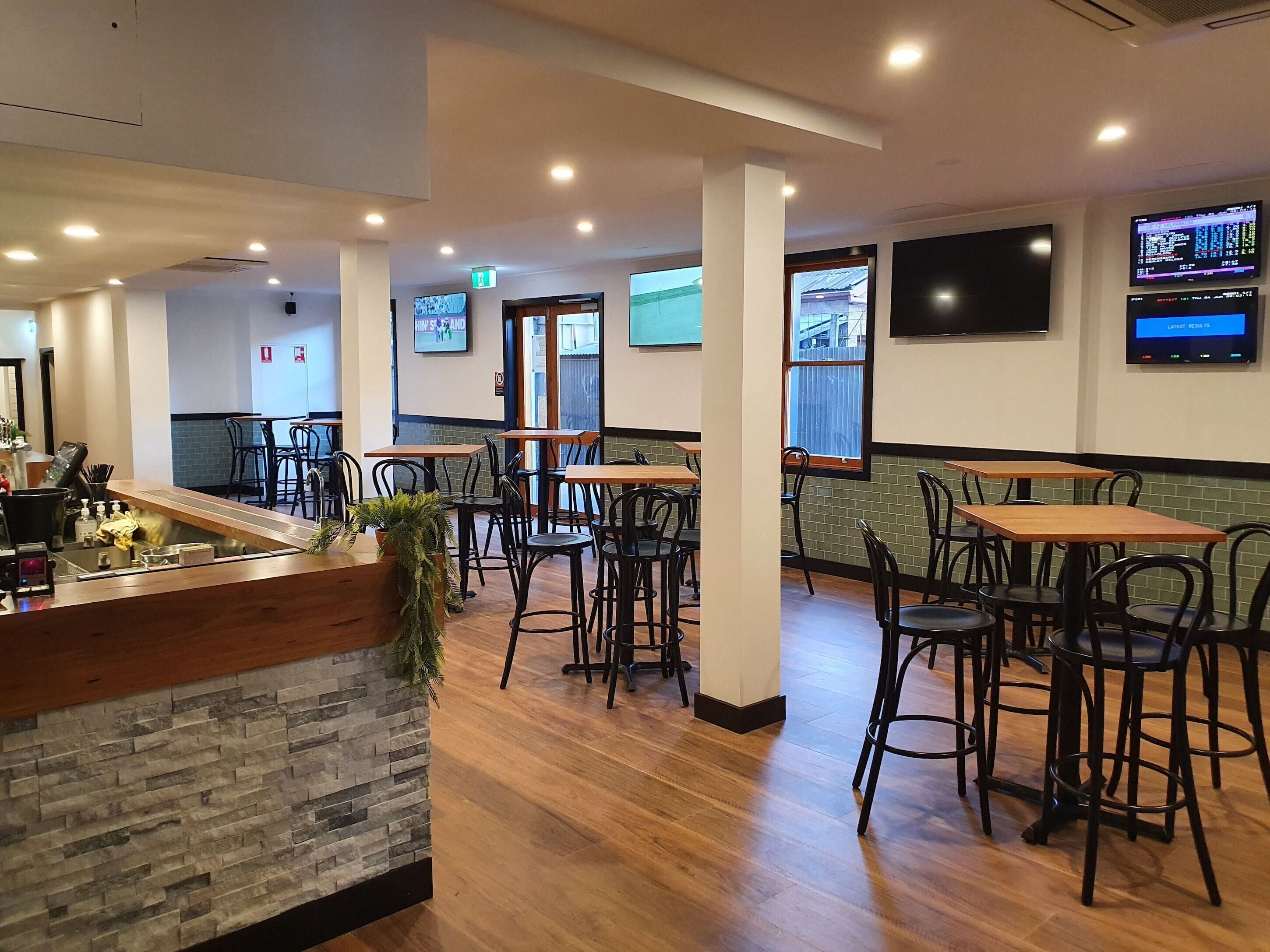 A restaurant interior with wooden tables and chairs, a stone accent wall, and multiple screens displaying content.