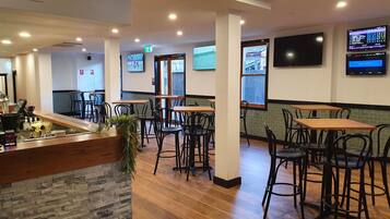 A restaurant interior with wooden tables and chairs, a stone accent wall, and multiple screens displaying content.