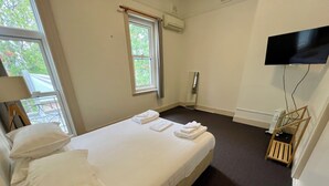 A hotel room with a bed, pillows, a window, an air conditioning unit, a television mounted on the wall, and a small wooden chair. - Empire Hotel Goulburn (Goulburn)