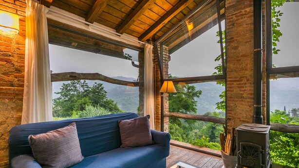 A cozy room with a blue sofa, large windows, and a wood-burning stove. - Cosy apartment for 2 guests with A/C, pool, WIFI, TV, patio and pets allowed (Pescia)