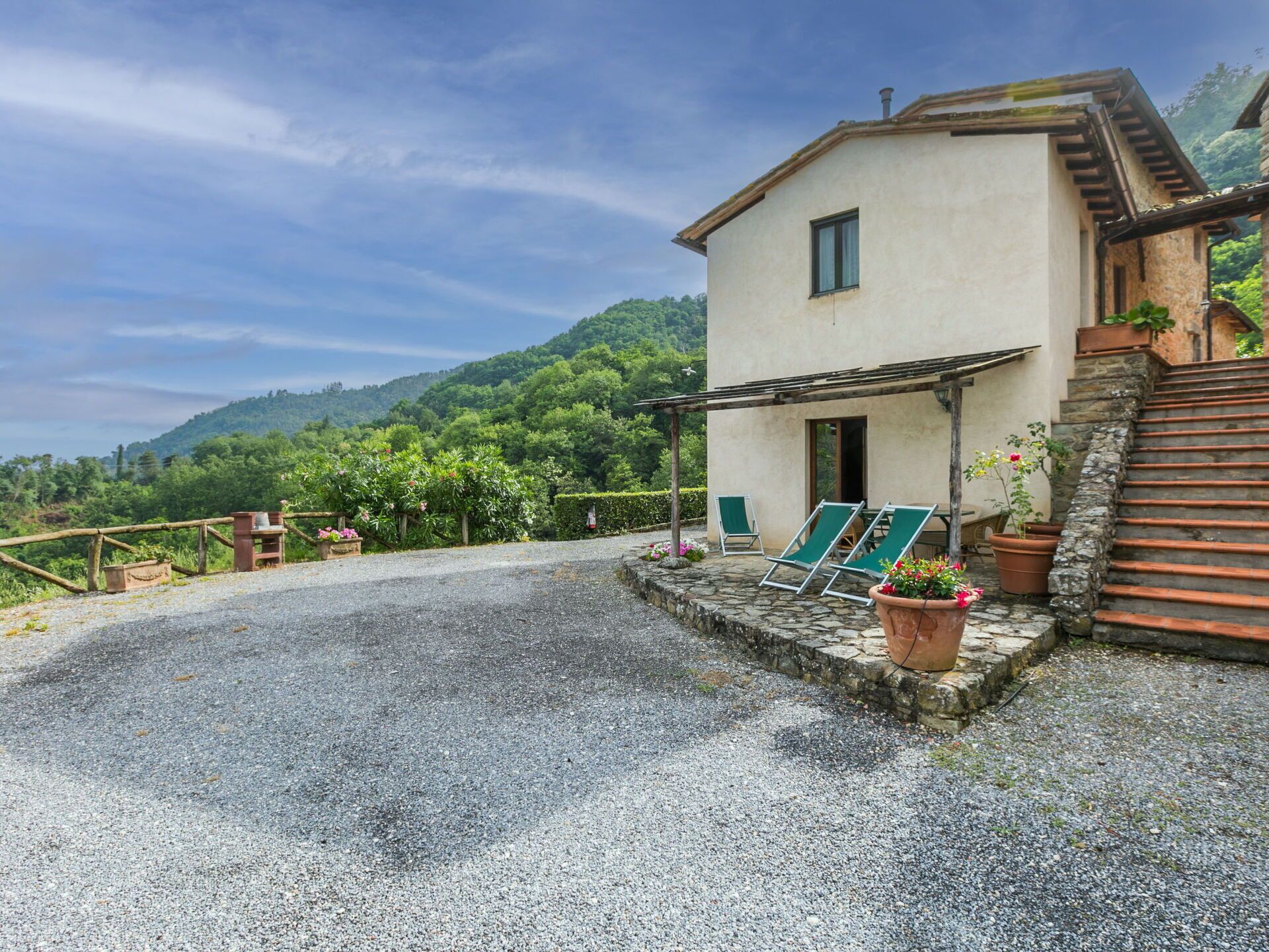 A two-story building with a gravel driveway, a wooden fence, and a stone staircase leading to a balcony.