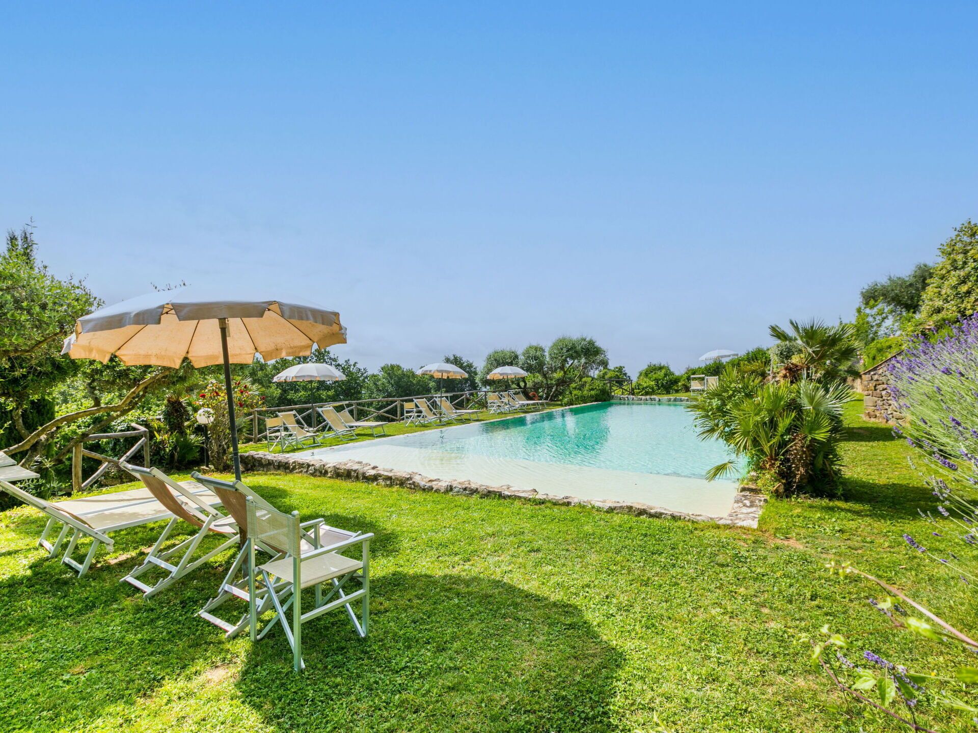 A swimming pool with lounge chairs and umbrellas, surrounded by greenery and a stone wall.