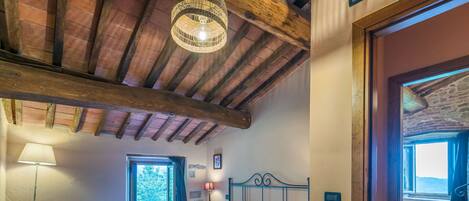 A bedroom with a bed, a nightstand, a lamp, a window, and a wooden ceiling.
