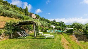 A pool area with lounge chairs and umbrellas, surrounded by lush greenery and a stone wall. - Cosy apartment for 4 people with WIFI, pool, TV and patio (Pescia)