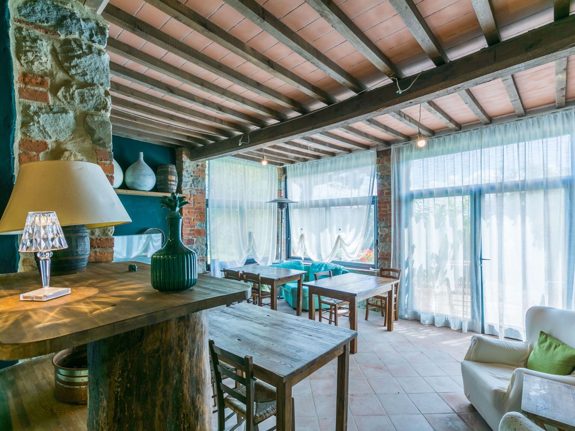 Un intérieur rustique avec des poutres apparentes, un mur en briques et un coin repas agrémenté de tables et de chaises en bois.