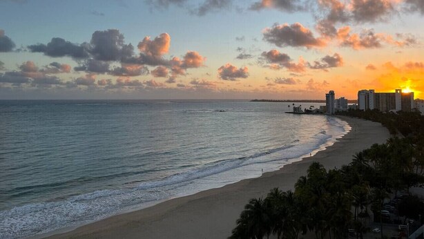 A beach with a sunset, ocean, and buildings in the background. - Beachfront in of Isla Verde W/D  Great value (Carolina)