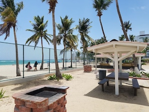 A beachside patio with a grill, benches, and a covered seating area.