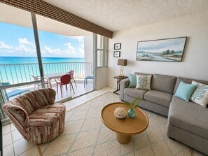 Ein Wohnzimmer mit einer Couch, einem Sessel, einem Couchtisch und Meerblick durch große Fenster.