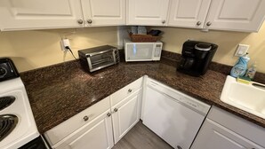 Una cocina compacta con armarios blancos, microondas, tostadora y lavavajillas.