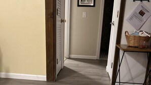 Un pasillo con suelo de madera, una puerta con marco blanco y una pared con dos cuadros enmarcados y una silueta de alce.