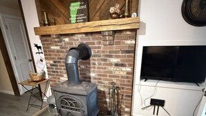 Una habitación con estufa de leña, chimenea de ladrillo, televisor montado y un cartel sobre la chimenea.