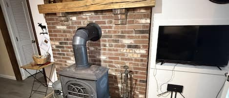 Una habitación con estufa de leña, chimenea de ladrillo, televisor montado y un cartel sobre la chimenea.