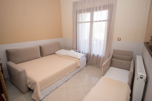 A room with a bed, a sofa, and a chair. There is a window with curtains.