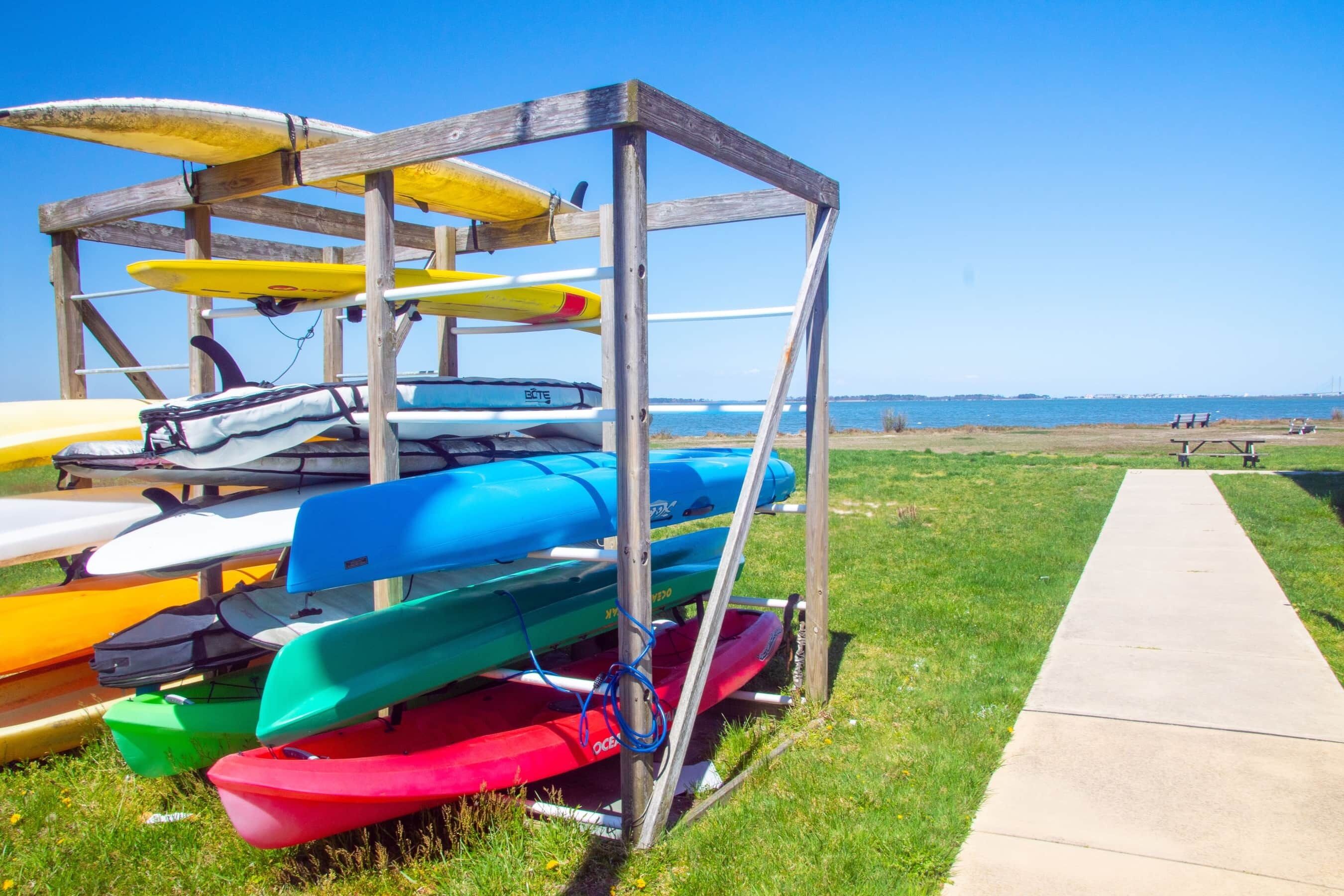 A wooden rack holding various kayaks and a concrete path leading to a beach.