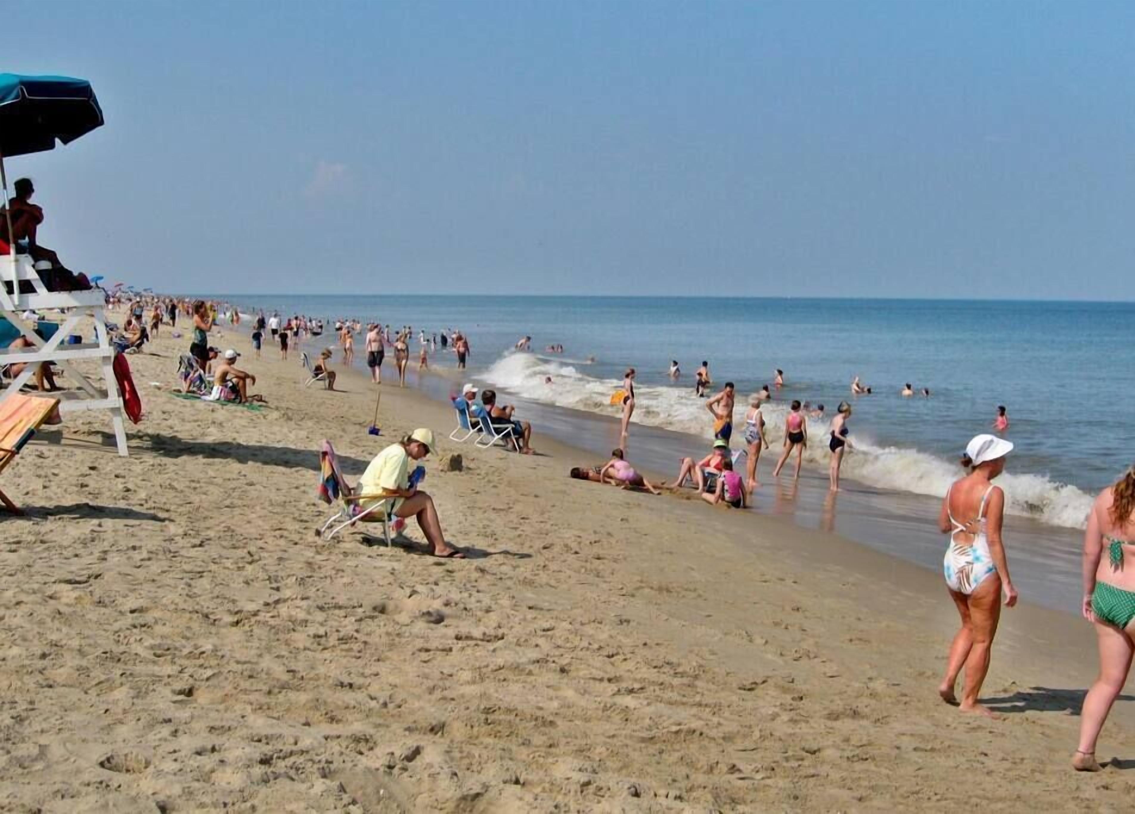 Une plage bondée où les gens se prélassent au soleil, nagent et se promènent le long du rivage.