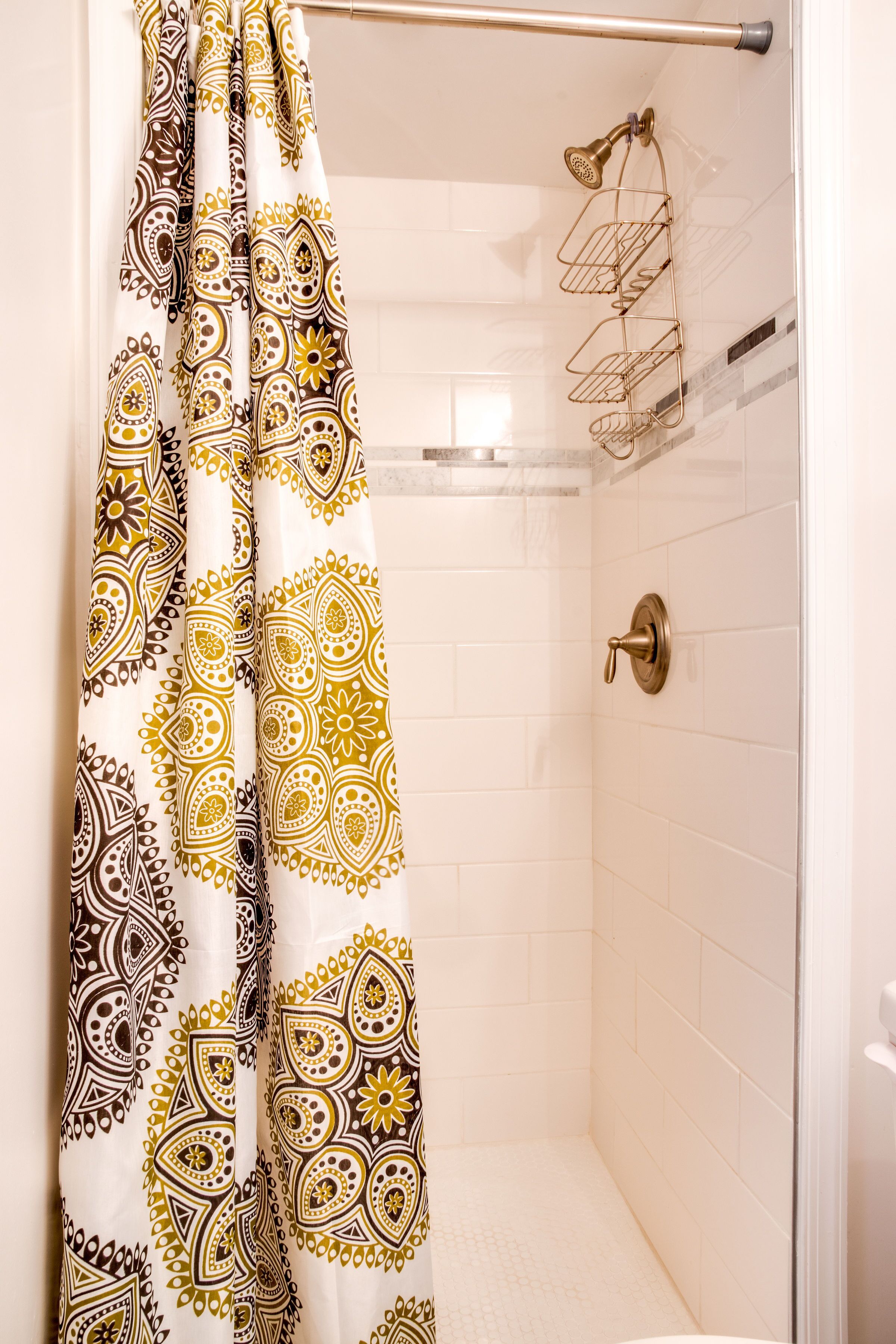 A shower area with a patterned shower curtain, a glass shower door, and a metal showerhead.