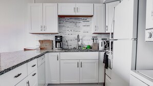 A modern kitchen with white cabinets, a granite countertop, and a coffee maker.