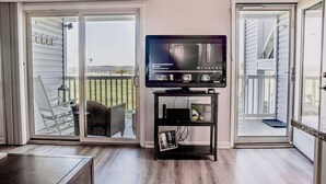 A living room with a television on a stand, a sliding glass door to a balcony, and a small table.