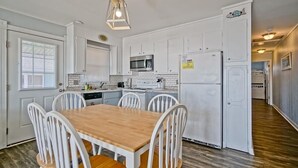 Una cocina compacta con armarios blancos, una mesa de comedor de madera y una lámpara colgante.