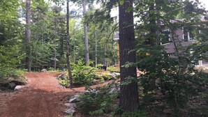 A forested area with a dirt path leading to a house. - Peaceful, family-friendly Maine getaway at newly built scenic lakefront cottage  (Clifton)